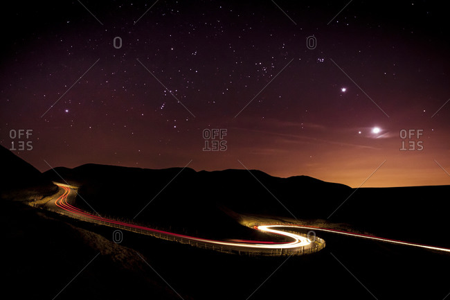 Light trails and stars cape with Venus, Jupiter, Orion and the moon clearly visible above a winding road in the Peak District National Park. Derbyshire, England, United Kingdom, Europe
