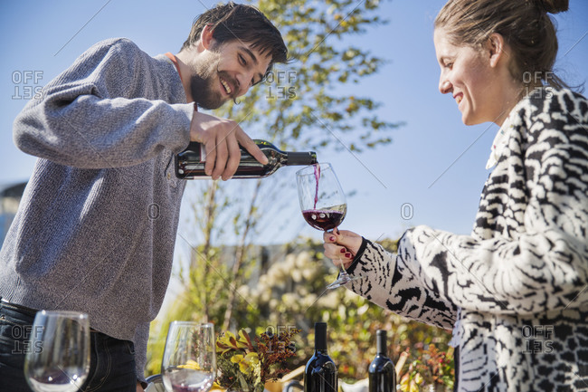 Young man pouring red wine to smiling woman