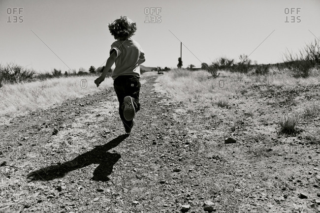 Back view of a boy running on a dirt road