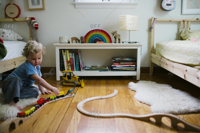 Toddler boy playing with classic wooden train set in kids room