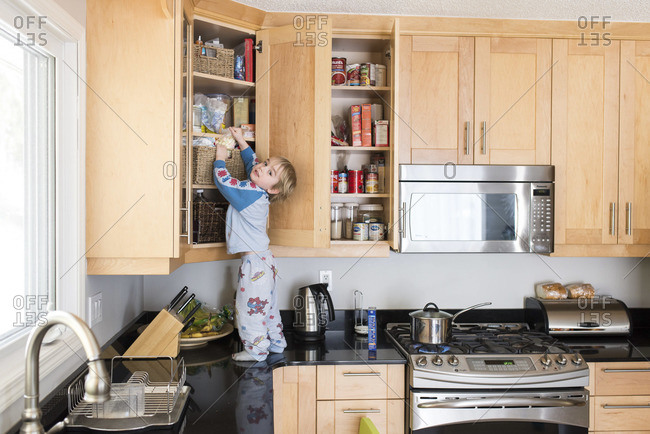 Toddler boy standing on kitchen counter and searching something in wall cabinet