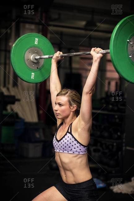 Woman doing shoulder press exercise with a weight bar inside a gym