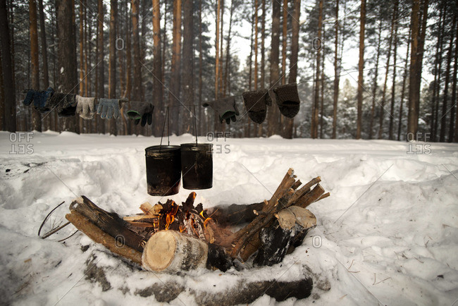 Two buckets and several pairs of gloves heat-up over an open fire in a snowy forest