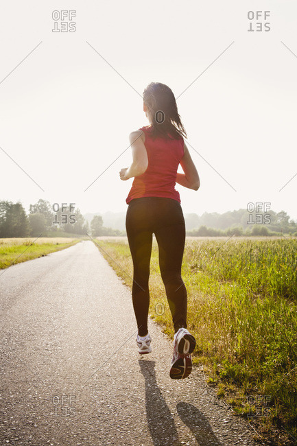 Rear view of young woman jogging on country road