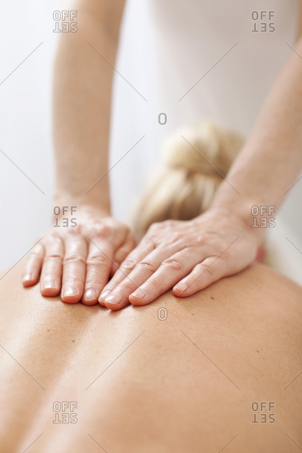 Rear view of a mid adult woman receiving back massage from mature therapist at health spa
