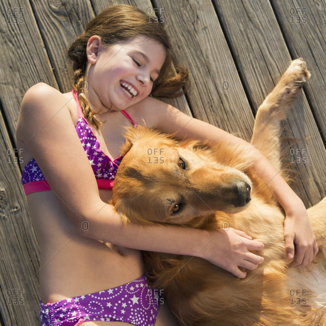 A girl in a bikini lying beside a golden retriever dog, viewed from above