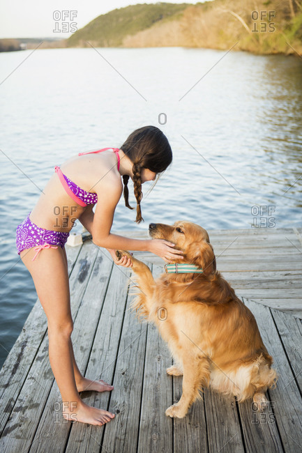 A girl in a bikini with a golden retriever dog lifting its paw up