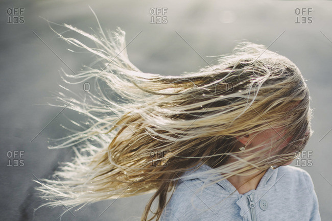 A blonde girl\'s hair blowing in the wind, obscuring her face