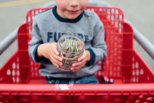 Boy sitting in a shopping cart with a money jar in his hands