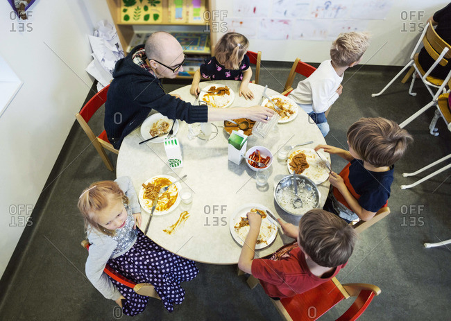 High angle view of kindergarten students and teacher having food at dining table