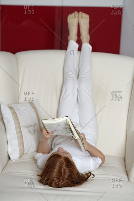 Girl lying on sofa with legs in the air reading a book