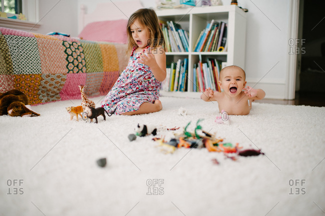 Older sister playing with plastic animals while a baby looks excited