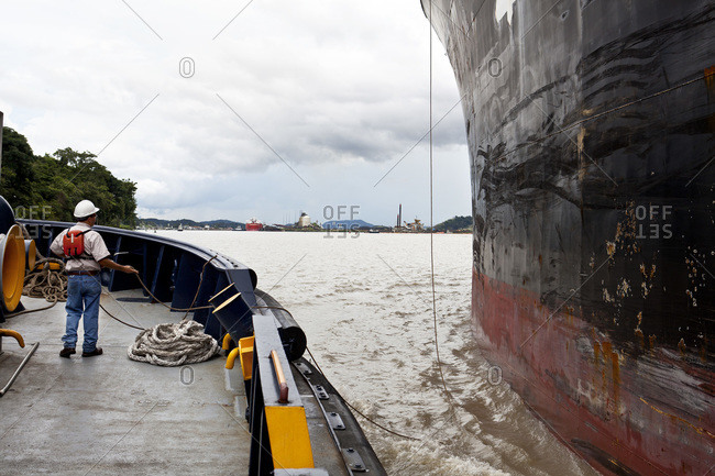 Crew member of a tugboat arranges his ropes while assisting a cargo ship through the Panama Canal