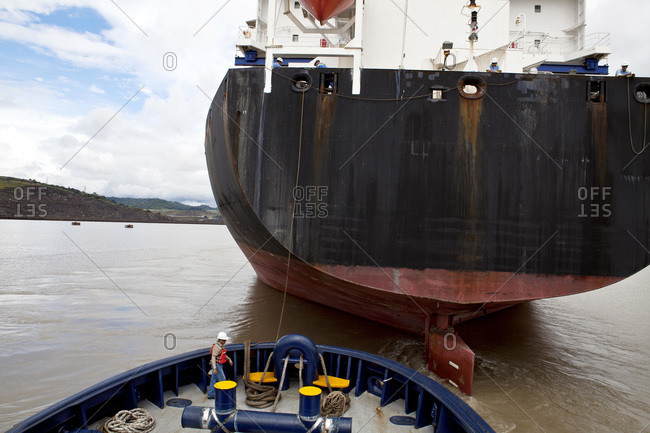 Crew member of a tugboat working with ropes while assisting a cargo ship and its transit of the Panama Canal