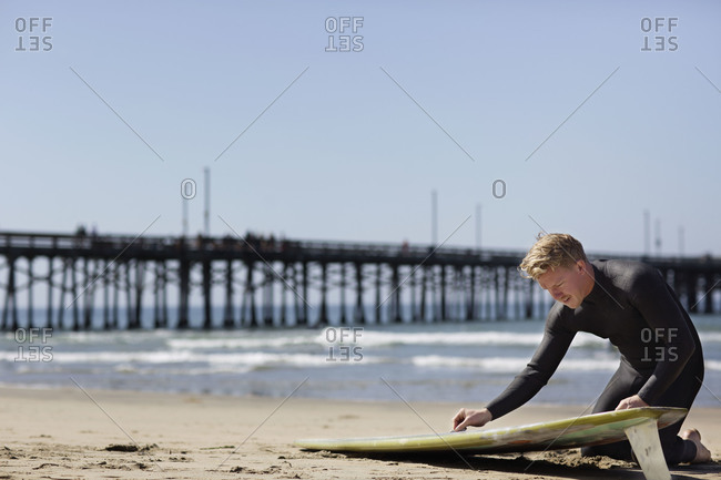 Man waxing a surfboard on a beach
