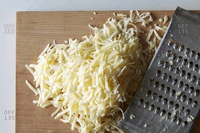 Top view of a pile of grated cheese next to a cheese grater on a cutting board