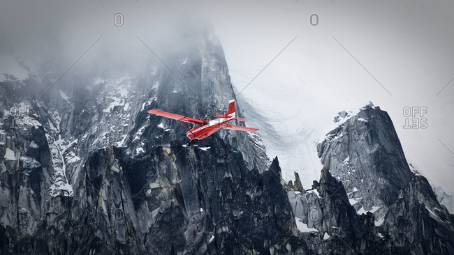 A red bush plane flies in front of a peak in Little Switzerland, Alaska Range