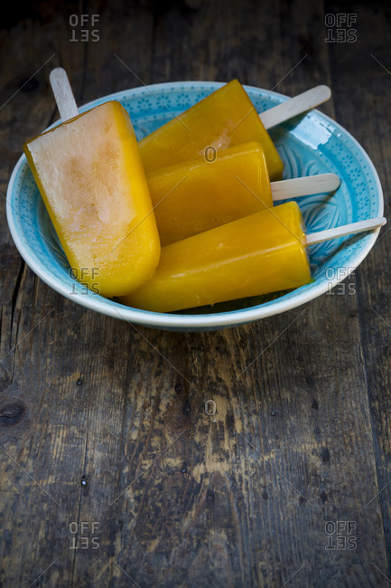Bowl of four mango apple ice cream lollies on dark wood