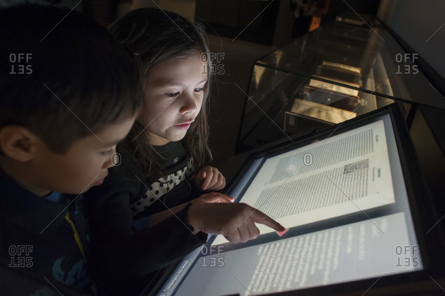 Twin children read a digital historical book at a museum