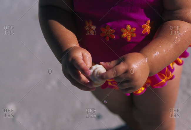 A toddler finds a shell on the beach.