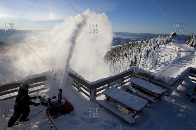 Worker using a snow blower to remove snow from the summit house deck