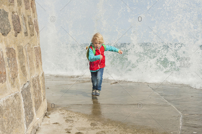 Excited boy standing at the pier with splashing water
