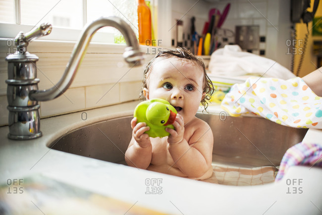 Baby girl playing with a duck toy in a sink
