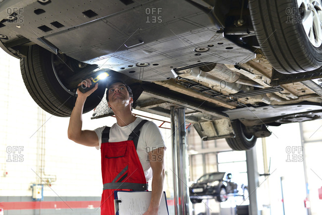 Car mechanic in a workshop checking underbody of a car