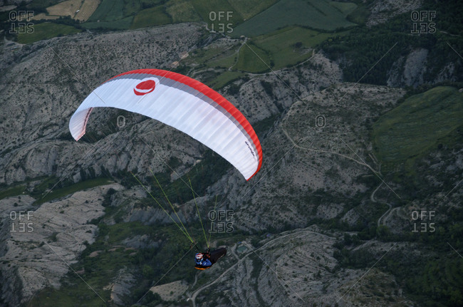 A paraglider flies above roads and rocky farmland in the Pyrenees, Spain