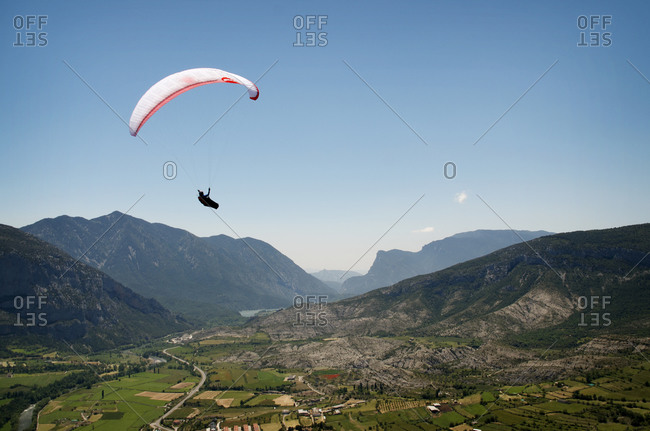 A paraglider pilot soars high above a populated valley in the Pyrenees, Spain.