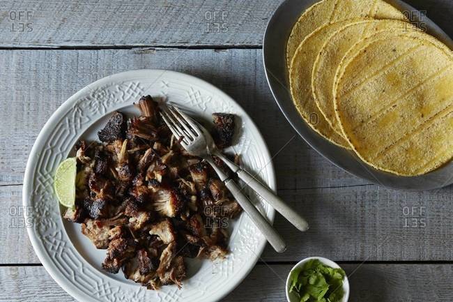 Top view of Mexican carnitas with lime wedge and tortillas