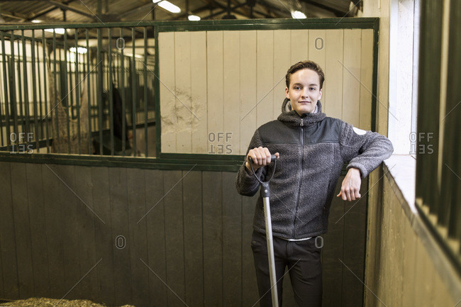 Portrait of confident young man with pitchfork in horse stable
