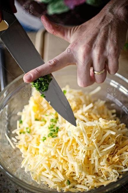 Person adding diced green peppers to a bowl of grated cheese