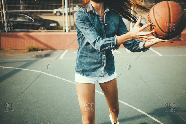 Woman in white shorts and denim shirt playing basketball