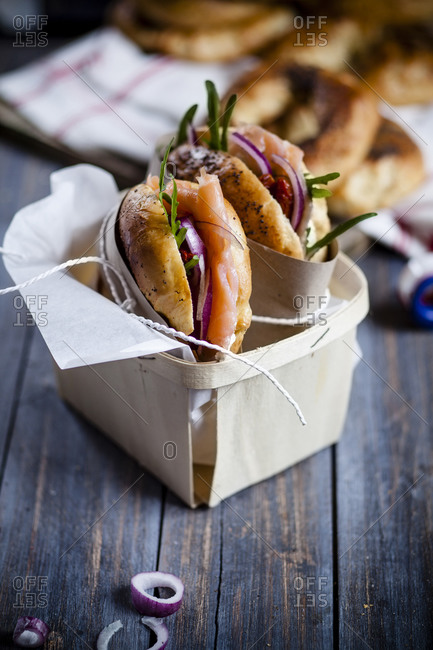 Two garnished home-baked bagels wrapped in paper standing in a box