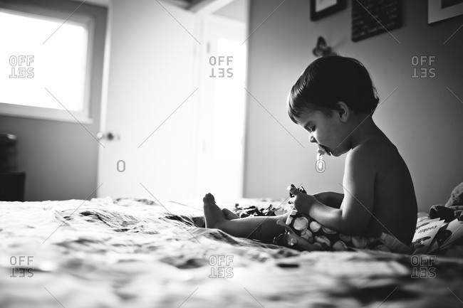 Boy sits on bed playing with toys