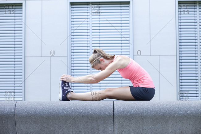 Young woman doing stretching exercise in front of facade of an office building