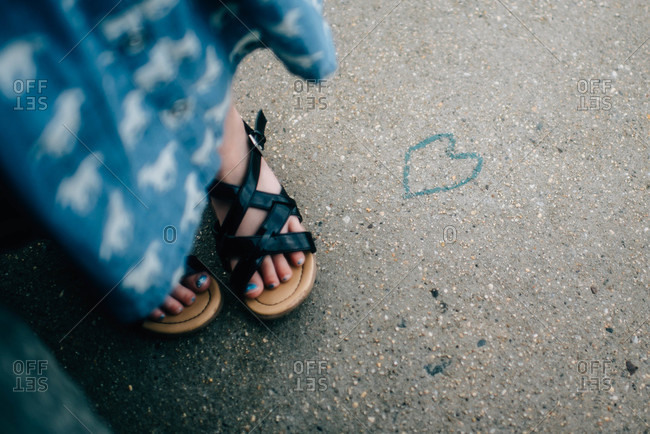 Close up of a girl\'s feet next to a heart drawing on the pavement