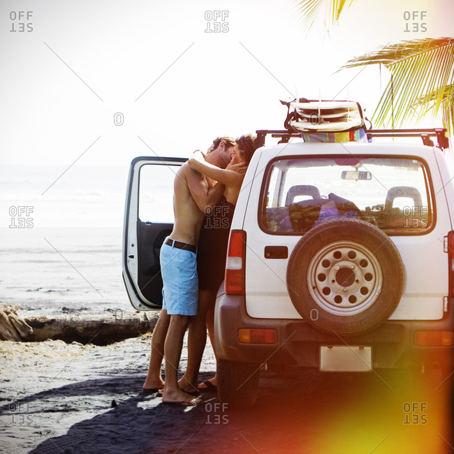 Young couple kissing by car on the beach