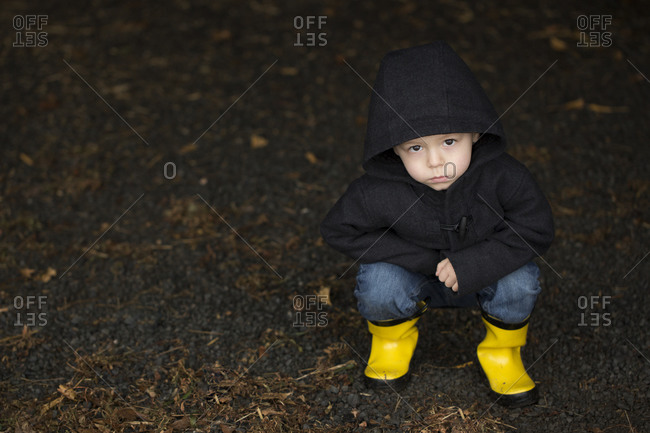 Young boy squatting in yellow rain 
