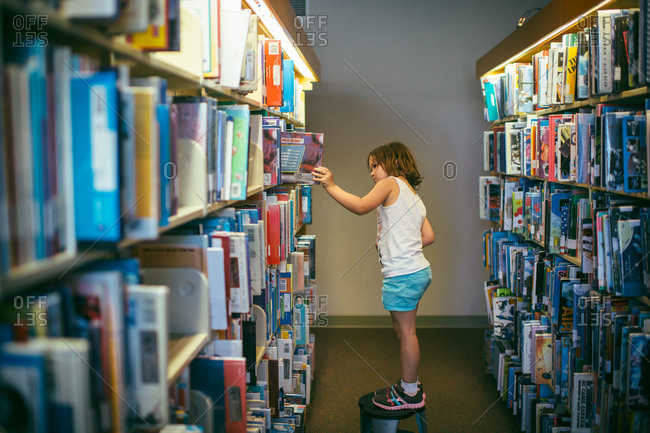 Young girl on a step stool looking at a library book