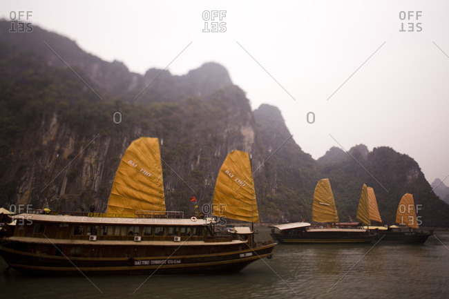 Sail boats in front of large limestone formation, Halong Bay, Vietnam