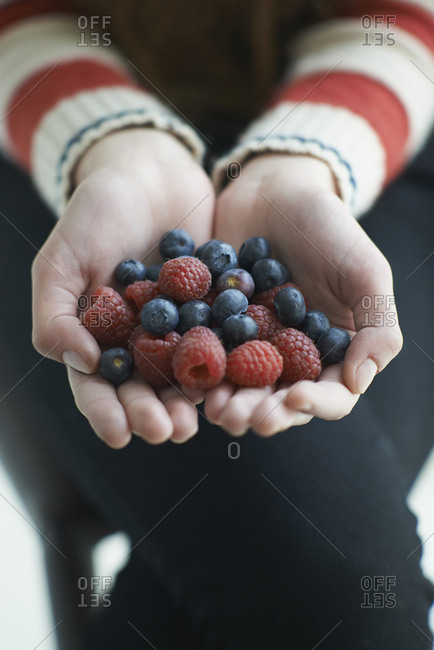 Close-up of girl\'s hands holding blue berries and raspberries
