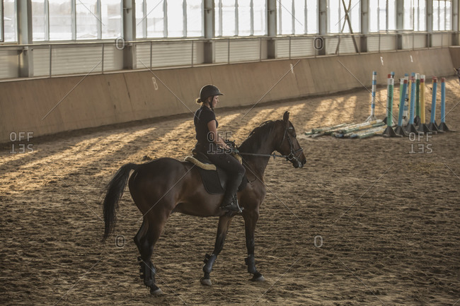 Side view of woman riding horse in training stable