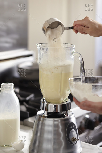 Person adding measured flour into electric blender