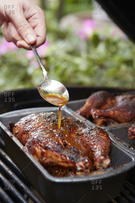 Man spooning gravy over a chicken on the grill