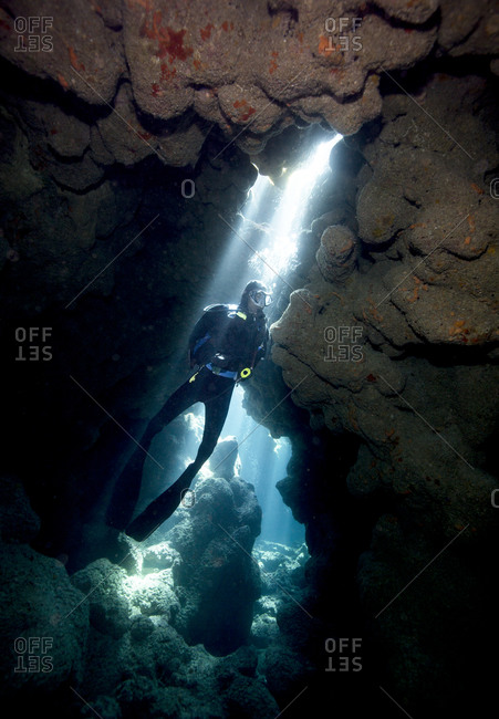 Crepuscular rays illuminate a scuba diver at Coral Caverns dive site