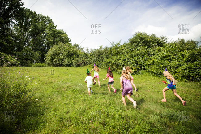 Children running uphill in birthday party hats