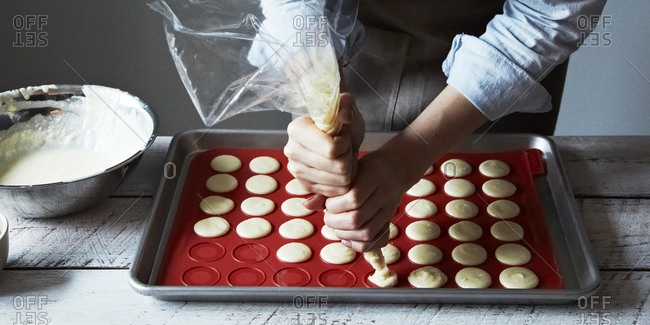 Close up of woman squeezing macaroon batter onto baking mat