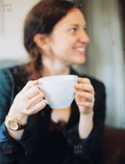 A woman holding a large white china cup and looking sideways smiling.